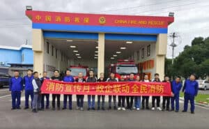 Fire rescue team holding a red banner in front of China Fire and Rescue station, promoting fire safety awareness.