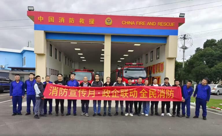 Fire rescue team holding a red banner in front of China Fire and Rescue station, promoting fire safety awareness.
